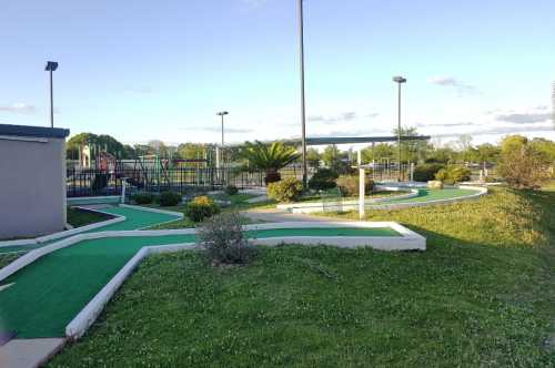 A mini-golf course with winding paths, green turf, and surrounding greenery under a clear blue sky.