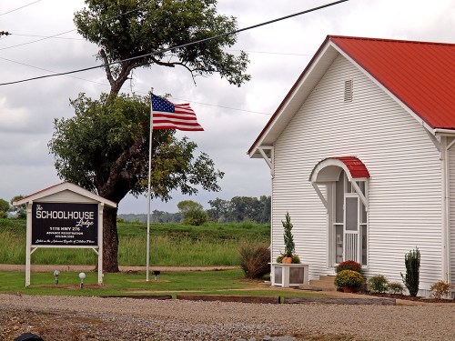 A white building with a red roof, featuring a sign for "The Schoolhouse" and an American flag nearby.