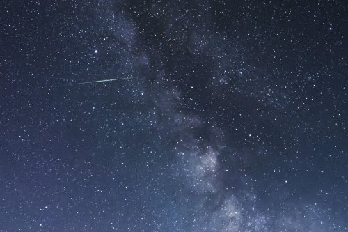 A starry night sky filled with countless stars and a bright meteor streaking across the Milky Way.