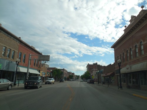 A quiet downtown street lined with historic buildings under a partly cloudy sky.