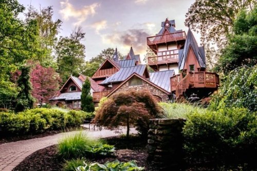 A charming, multi-roofed house surrounded by lush greenery and colorful trees, with a winding stone pathway in the foreground.