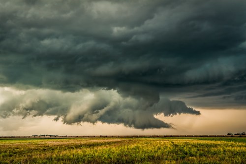Dark, swirling storm clouds loom over a grassy field, creating a dramatic and ominous sky.