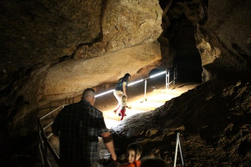A family explores a cave, with a child walking ahead and a parent following, illuminated by soft lights.