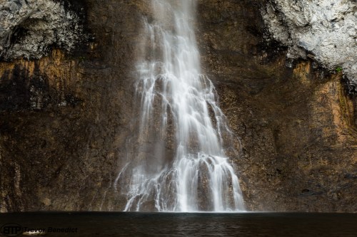 A cascading waterfall flows down a rocky cliff into a serene pool below, surrounded by natural textures.