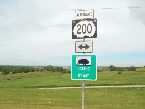 A road sign indicating Alternate 200 and a Scenic Byway with a silhouette of a bison, set against a green landscape.
