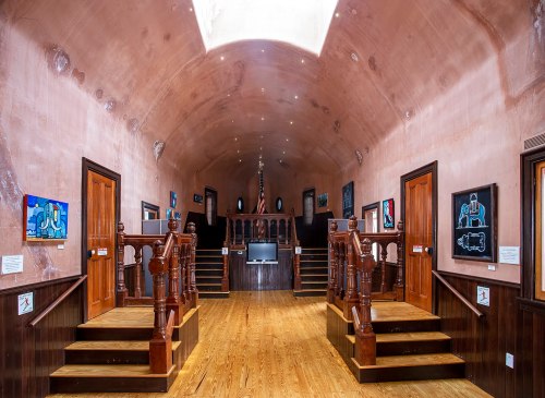 Interior of a spacious hall with wooden stairs, art on the walls, and a skylight illuminating the space.