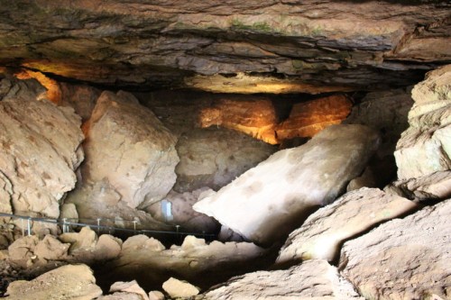A dimly lit cave interior with large rock formations and a pathway visible among the boulders.