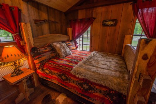 Cozy rustic bedroom with wooden walls, a patterned bedspread, a fur throw, and warm lighting from a bedside lamp.