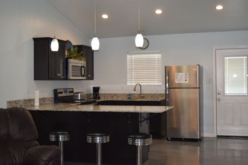 Modern kitchen with black cabinets, stainless steel appliances, granite countertops, and bar stools. Bright and spacious.