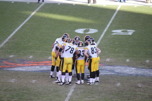 A group of Pittsburgh Steelers players huddled on the field during a game, wearing their black and gold uniforms.