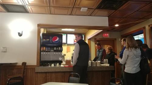 A group of people at a restaurant counter, with a Pepsi machine and menu visible in the background.