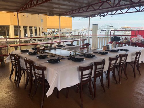 A large dining table set with black plates and utensils, overlooking a marina with boats in the background.