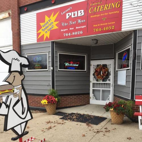 Exterior of Larson's Pub with a chef sign, flowers, and a welcoming entrance. Signs advertise food and beverages.