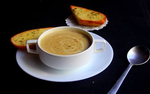 A bowl of creamy soup with a swirl, accompanied by two slices of garlic bread on a white plate.