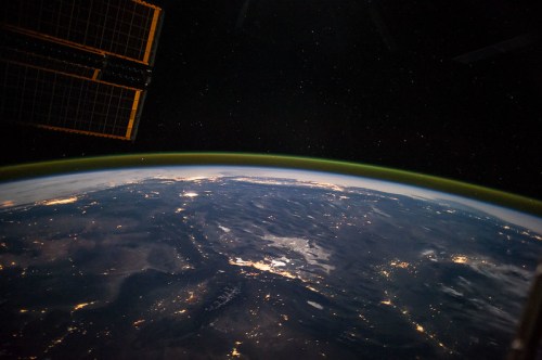 View of Earth from space, showcasing a curved horizon, city lights, and a starry night sky.
