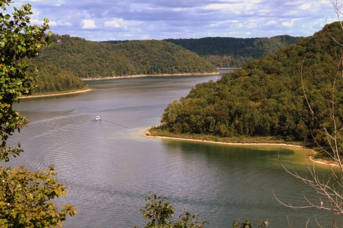 A serene river winding through lush green hills under a partly cloudy sky, with a small boat on the water.