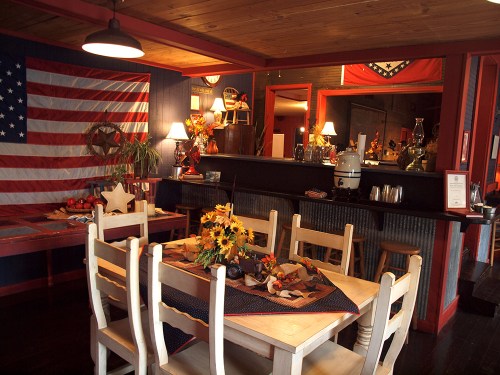 Cozy dining area with a wooden table, sunflowers, and American flags on the walls, creating a warm, inviting atmosphere.