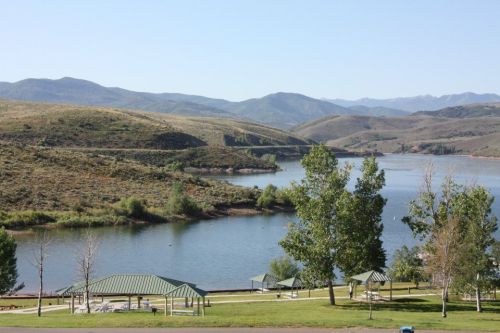 Scenic view of a calm lake surrounded by green hills and mountains, with picnic shelters in the foreground.