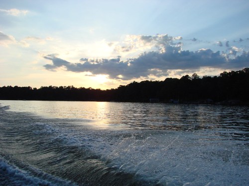 Sunset over a calm lake, with rippling water and clouds reflecting the warm colors of the sky.