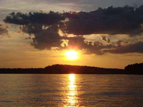 A serene sunset over calm waters, with clouds reflecting warm hues of orange and gold.