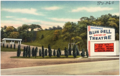 A vintage postcard of the Blue Dell Drive-In Theatre entrance, featuring a scenic landscape and movie listings.