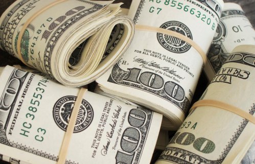Stacks of rolled hundred-dollar bills secured with rubber bands, arranged on a flat surface.