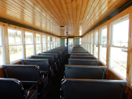 Interior of a vintage train car with wooden paneling and rows of empty seats along the windows.