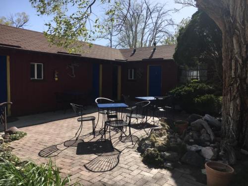 A cozy outdoor patio with metal tables and chairs, surrounded by greenery and rustic buildings.