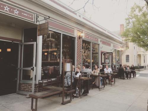 Outdoor dining scene at a bistro with patrons seated at tables along the sidewalk, enjoying a pleasant evening.