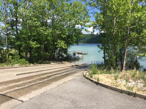 A serene lake view with a boat ramp, surrounded by green trees and calm water under a clear blue sky.