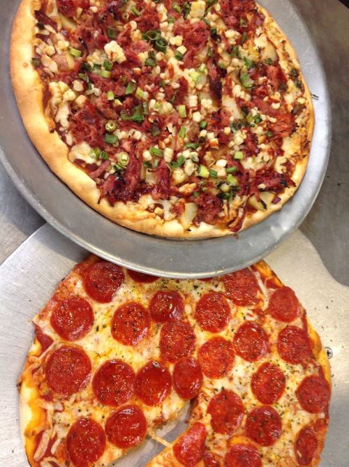 Two pizzas on a metal tray: one topped with pepperoni and cheese, the other with ham, pineapple, and green onions.