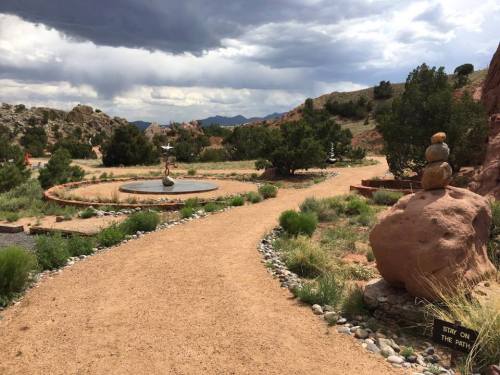 A winding path through a rocky landscape with stacked stones and greenery under a cloudy sky.