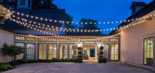 A beautifully lit outdoor venue at dusk, featuring string lights and elegant architecture.