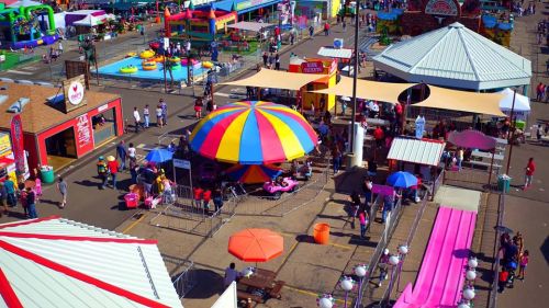 A vibrant carnival scene with colorful tents, rides, food stalls, and people enjoying various attractions.