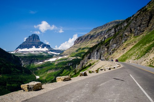A scenic mountain road with lush green hills and a prominent peak under a clear blue sky.