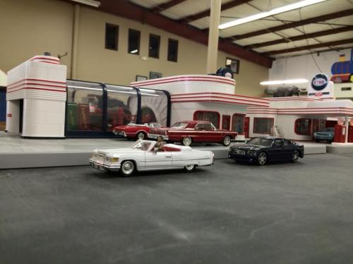 A model gas station with vintage cars parked outside, featuring a retro design and bright colors.