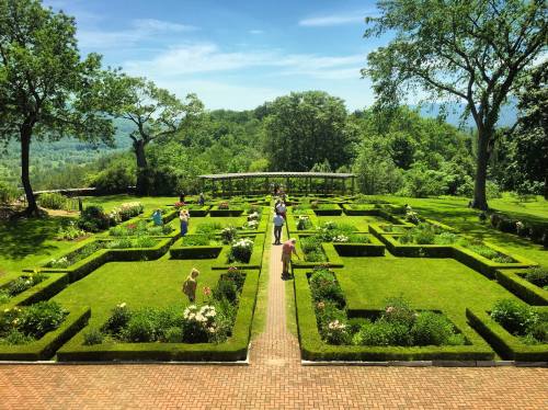 A lush garden with neatly trimmed hedges and colorful flowers, featuring people walking and enjoying the scenery.
