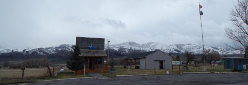A small building with a flag, surrounded by mountains and a cloudy sky, in a rural landscape.