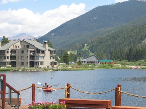 A serene lake scene with a kayaker, mountains in the background, and buildings along the shore.
