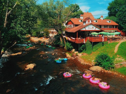 A scenic view of a river with colorful inner tubes floating by a rustic restaurant surrounded by lush greenery.