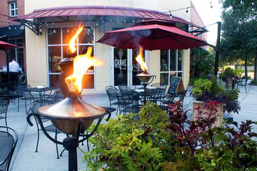 Outdoor dining area with flaming torches, umbrellas, and colorful plants in front of a restaurant named "Crave."