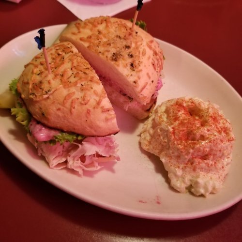 A sandwich with sliced turkey and lettuce on a toasted bun, served with a side of creamy potato salad.