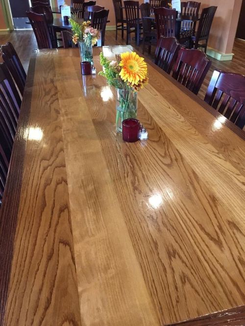 A long wooden dining table with two vases of flowers and candles, surrounded by wooden chairs in a cozy restaurant.