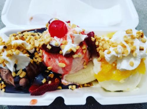 A dessert dish with three scoops of ice cream topped with whipped cream, nuts, a cherry, and chocolate sauce.