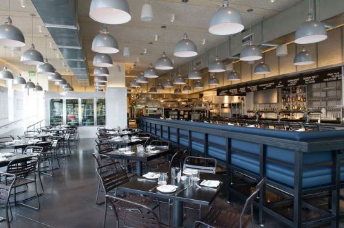 Modern restaurant interior with a bar, black tables, and pendant lighting, featuring a spacious and inviting atmosphere.
