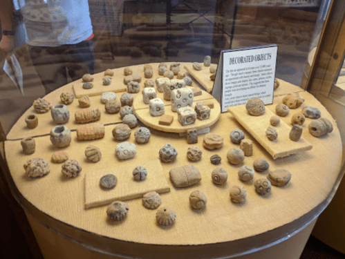 A display of various decorated clay objects in a museum, arranged on a circular table with a descriptive sign.
