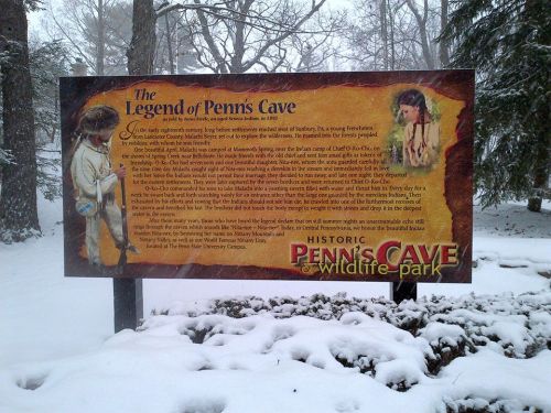 Sign about the Legend of Penn's Cave, featuring historical information, surrounded by snow-covered trees.