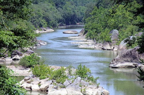 A serene river flows through a lush green landscape, surrounded by large rocks and trees.