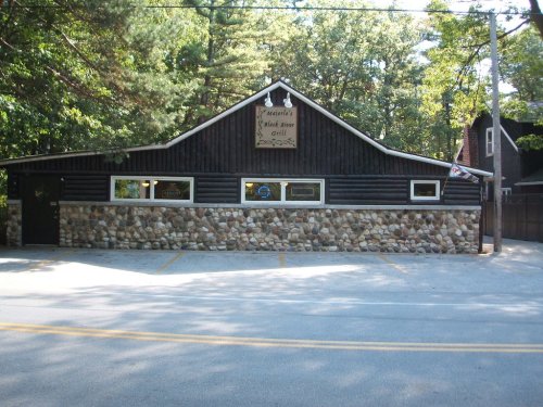 A rustic building with a stone facade and wooden upper section, surrounded by trees, serving as a grill restaurant.