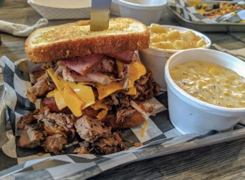 A hearty sandwich stacked with meats and cheese, served with sides of macaroni and cheese and corn chowder.